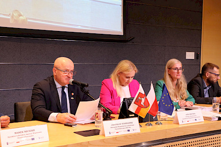 Stół konferencyjny przy którym siedzą cztery osoby. W środku dwie kobiety