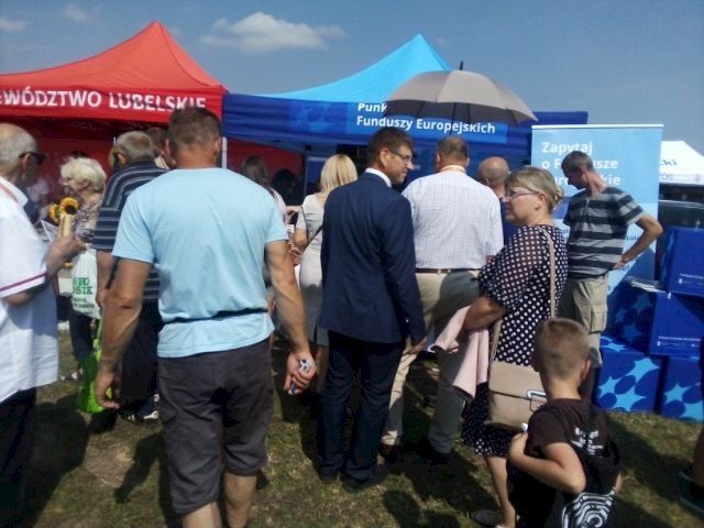 Grupa kilkunastu osób, mężczyzn i kobiet stojący przed namiotem Punktu Informacyjnego Funduszy Europejskich