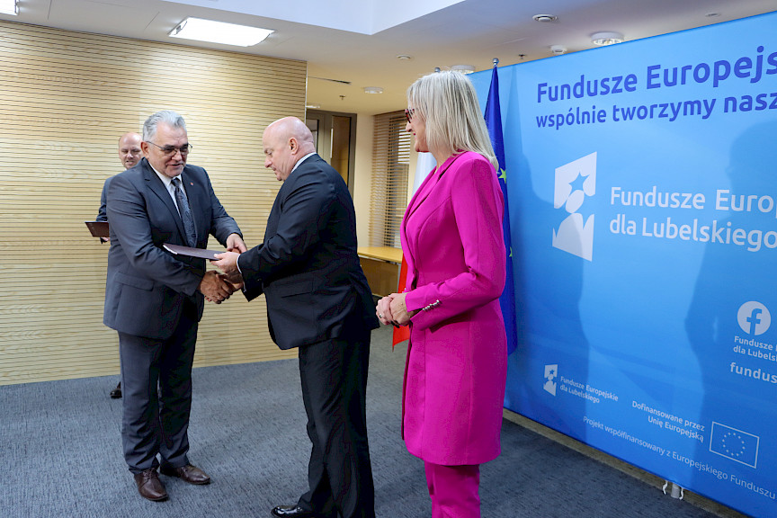 Marszałek Jarosław Stawiarki oraz radna Anna Baluch wręczają na tle ścianki Fundusze Europejskie wspólnie tworzymy naszą przyszłość, umowę Beneficjentowi na realizację unijnej inwestycji.