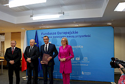 Pamiątkowe zdjęcie marszałka Jarosława Stawiarskiego oraz radnej Anny Baluch w towarzystwie Beneficjenta, któremu wcześniej wręczyli umowę na realizację inwestycji. Wszyscy stoją na tle ścianki ścianki Fundusze Europejskie wspólnie tworzymy naszą przyszłość oraz na tle flagi Polski i UE.