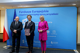 Pamiątkowe zdjęcie marszałka Jarosława Stawiarskiego oraz radnej Anny Baluch w towarzystwie Beneficjenta, któremu wcześniej wręczyli umowę na realizację inwestycji. Wszyscy stoją na tle ścianki ścianki Fundusze Europejskie wspólnie tworzymy naszą przyszłość oraz na tle flagi Polski i UE.