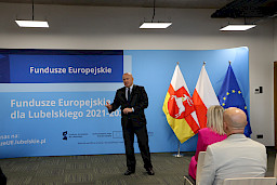 Marszałek Jarosław Stawiarski na tle niebieskiej ścianki Fundusze Europejskie dla Lubelskiego 2021-2027 i flagi województwa i Polski rozpoczyna konferencję