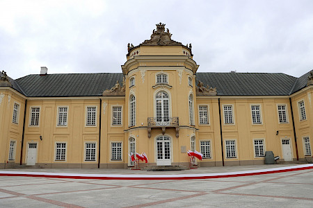 Widok na fasadę Pałacu Potockich w Radzyniu Podlaskim. Na pierwszym planie widać rozciągniętą biało czerwoną wstęgę