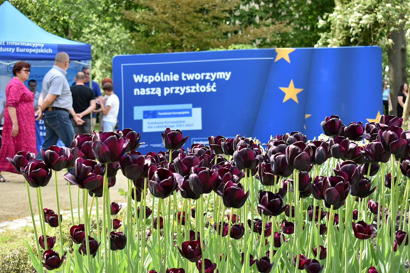 Piknik w Woli Okrzejskiej na pierwszym pani dwoje ludzi trzymających się za ręce. Mężczyzn a kontuszu. W tle widoczny narożnik zabytkowego dworku