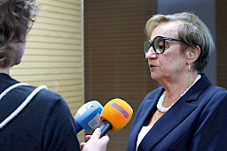 Elegancka kobieta w okularach udziela wywiadu lokalnym radiostacjom.