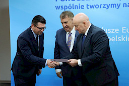 Marszałek Województwa Lubelskiego, Pan Jarosław Stawiarski na tle ścianki promocyjnej Fundusze Europejskie dla Lubelskiego wręcza umowę dwóm Beneficjentom