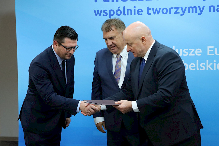 Marszałek Województwa Lubelskiego, Pan Jarosław Stawiarski na tle ścianki promocyjnej Fundusze Europejskie dla Lubelskiego wręcza umowę dwóm Beneficjentom