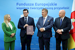Marszałek Województwa Lubelskiego, Pan Jarosław Stawiarski wraz z Panią Anną Brzyską, Dyrektor Departamentu Zarządzania Programami Regionalnymi z Beneficjentami, dwoma mężczyznami w garniturach pozują po wręczeniu umowy na tle ścianki promocyjnej Fundusze Europejskie dla Lubelskiego