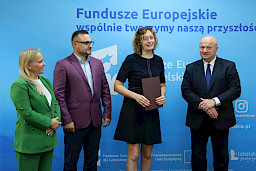 Marszałek Województwa Lubelskiego, Pan Jarosław Stawiarski wraz z Panią Anną Brzyską, Dyrektor Departamentu Zarządzania Programami Regionalnymi pozują  z Beneficjentami, kobietą i mężczyzną na tle ścianki promocyjnej  Fundusze Europejskie dla Lubelskiego