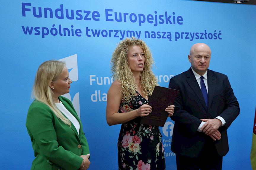 Marszałek Województwa Lubelskiego, Pan Jarosław Stawiarski wraz z Panią Anną Brzyską, Dyrektor Departamentu Zarządzania Programami Regionalnymi pozują  z Beneficjentką na tle ścianki promocyjnej  Fundusze Europejskie dla Lubelskiego