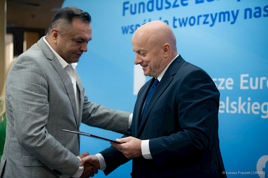 Marszałek Województwa Lubelskiego, Pan Jarosław Stawiarski wręcza umowę i ściska dłoń Beneficjenta na tle ścianki promocyjnej  Fundusze Europejskie dla Lubelskiego