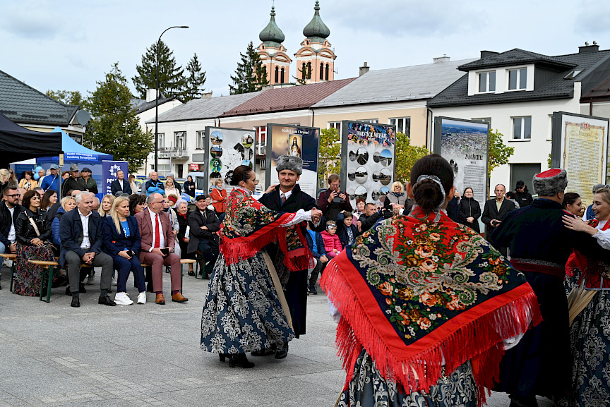 Rodzinny Piknik Europejski w Biłgoraju. Na pierwszym planie tańczący zespół ludowy. W oddali siedzą zaproszeni goście