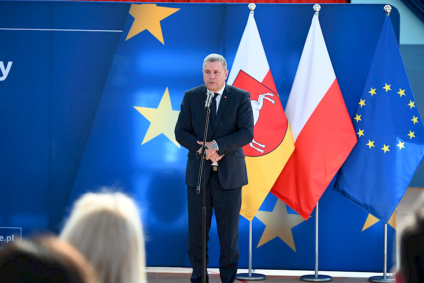Uroczyste wręczenie umów z Działania 10.4 w Radzyniu Podlaskim w dniu 21.10.2024 r. Starosta Radzyński na tle ścianki funduszy europejskich przemawia do zgromadzonych gości.