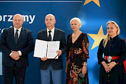 Uroczyste wręczenie umów z Działania 10.4 w Radzyniu Podlaskim w dniu 21.10.2024 r. Na tle ścianki funduszy europejskich stoi Marszałek Jarosław Stawiarski oraz beneficjent z wręczoną umową.