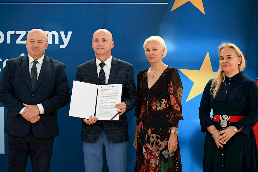 Uroczyste wręczenie umów z Działania 10.4 w Radzyniu Podlaskim w dniu 21.10.2024 r. Na tle ścianki funduszy europejskich stoi Marszałek Jarosław Stawiarski oraz beneficjent z wręczoną umową.