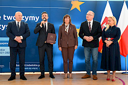 Uroczyste wręczenie umów z Działania 10.4 w Radzyniu Podlaskim w dniu 21.10.2024 r. Na tle ścianki funduszy europejskich stoi Marszałek Jarosław Stawiarski oraz beneficjent z wręczoną umową.