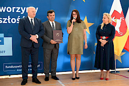 Uroczyste wręczenie umów z Działania 10.4 w Radzyniu Podlaskim w dniu 21.10.2024 r. Na tle ścianki funduszy europejskich stoi Marszałek Jarosław Stawiarski oraz beneficjent z wręczoną umową.