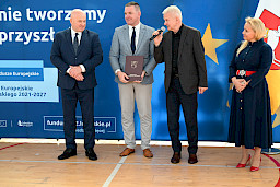 Uroczyste wręczenie umów z Działania 10.4 w Radzyniu Podlaskim w dniu 21.10.2024 r. Na tle ścianki funduszy europejskich stoi Marszałek Jarosław Stawiarski oraz beneficjent z wręczoną umową.