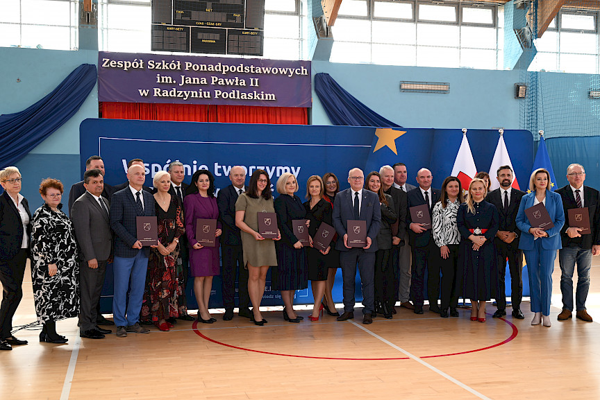 Uroczyste wręczenie umów z Działania 10.4 w Radzyniu Podlaskim w dniu 21.10.2024 r. Na tle ścianki funduszy europejskich stoi Marszałek Jarosław Stawiarski oraz beneficjenci z wręczonymi umowami