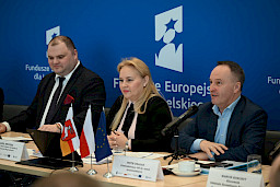 XVII Posiedzenie grup roboczych działających przy Komitecie Monitorującym Fundusze Europejskie dla Lubelskiego 2021-2027, trójka prezydium siedząca za stołem, w tle ścianka Funduszy Europejskich.
