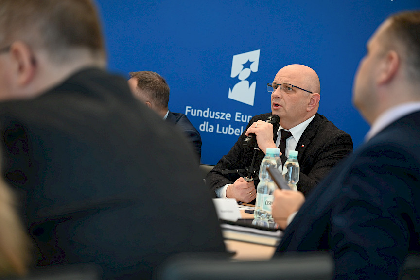 XVII Posiedzenie grup roboczych działających przy Komitecie Monitorującym Fundusze Europejskie dla Lubelskiego 2021-2027,członek prezydium zabiera głos, w tle ścianka Funduszy Europejskich.