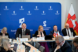 XVII Posiedzenie grup roboczych działających przy Komitecie Monitorującym Fundusze Europejskie dla Lubelskiego 2021-2027, trójka prezydium siedząca za stołem, w tle ścianka Funduszy Europejskich.