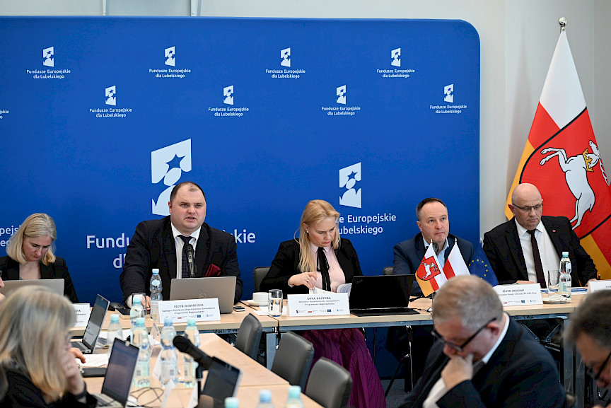 XVII Posiedzenie grup roboczych działających przy Komitecie Monitorującym Fundusze Europejskie dla Lubelskiego 2021-2027, trójka prezydium siedząca za stołem, w tle ścianka Funduszy Europejskich.