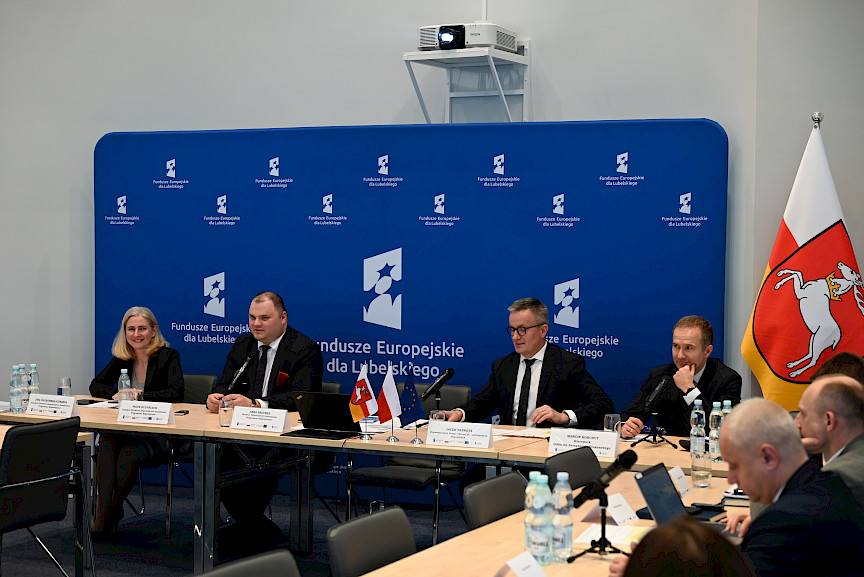 XVII Posiedzenie grup roboczych działających przy Komitecie Monitorującym Fundusze Europejskie dla Lubelskiego 2021-2027, na pierwszym planie prezydium, w tle ścianka Funduszy Europejskich.