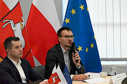 XXXVIII Posiedzenie Komitetu Monitorującego Regionalny Program Operacyjny Województwa Lubelskiego, członek prezydium zabiera głos, w tle flagi.