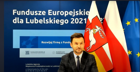 Prowadzący siedzi przy stole w tle ścianka z napisem Fundusze Europejskie dla Lubelskiego