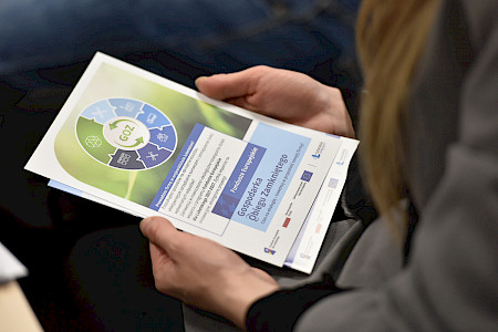 zdjecie przedsitawia dłonie trzymające ulotkę kolorach zieleni i niebieskiego z napisem GOZ, Gospodarka Obiegu Zamkniętego