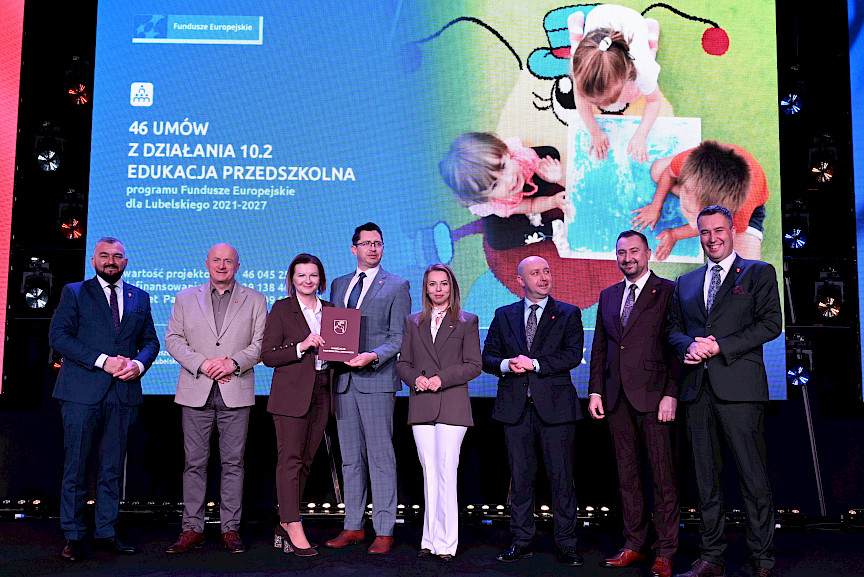 Zdjęcie Zarządu Województwa Lubelskiego z beneficjentami projektu. Kobieta i mężczyzna wspólnie trzymają teczkę z umową.