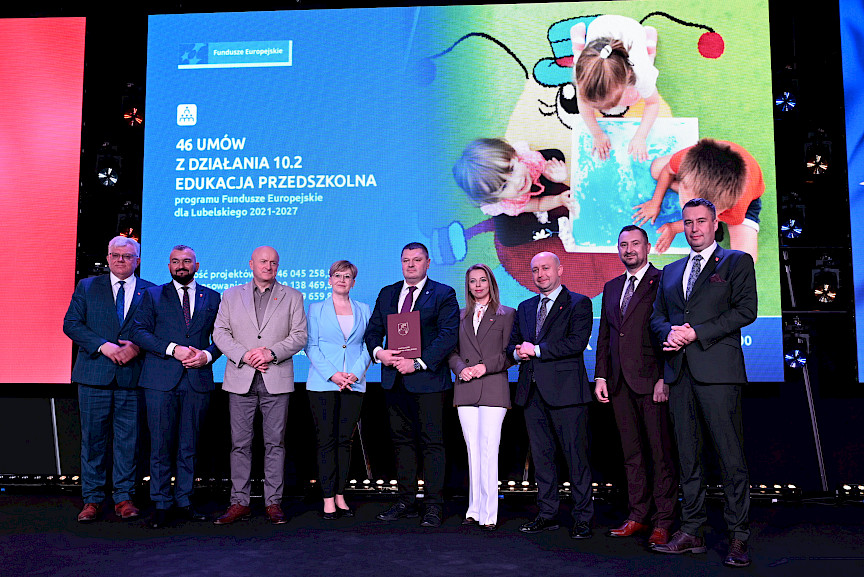 Zdjęcie Zarządu Województwa Lubelskiego z beneficjentami projektu. Mężczyzna trzyma teczkę z umową.