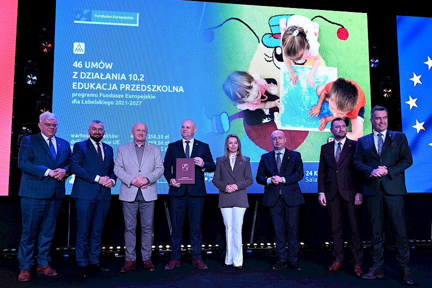 Zdjęcie Zarządu Województwa Lubelskiego z beneficjentami projektu. Mężczyzna trzyma teczkę z umową.