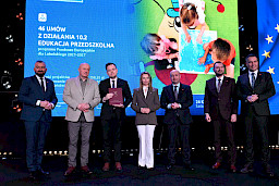 Zarząd Województwa Lubelskiego pozuje do zdjęcia z beneficjentem projektu. Mężczyzna trzyma teczkę w umową.