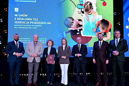 Zarząd Województwa Lubelskiego pozuje do zdjęcia z beneficjentką projektu. Kobieta trzyma teczkę w umową.