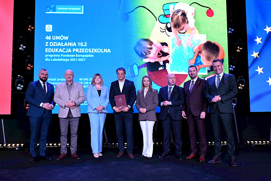 Zarząd Województwa Lubelskiego pozuje do zdjęcia z beneficjentami projektu. Mężczyzna trzyma teczkę w umową.