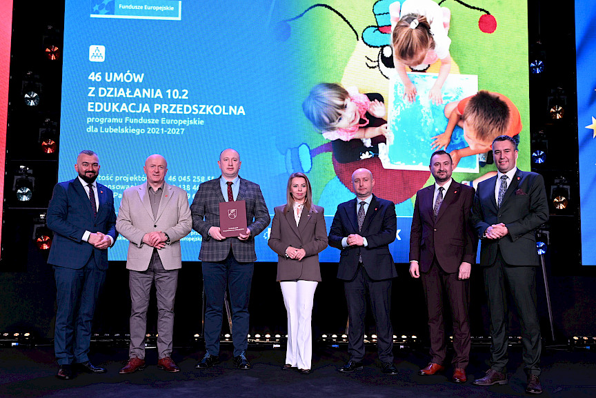 Zarząd Województwa Lubelskiego pozuje do zdjęcia z beneficjentem projektu. Mężczyzna trzyma teczkę w umową.
