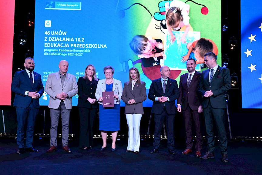 Zarząd Województwa Lubelskiego pozuje do zdjęcia z beneficjentkami projektu. Kobieta trzyma teczkę w umową.