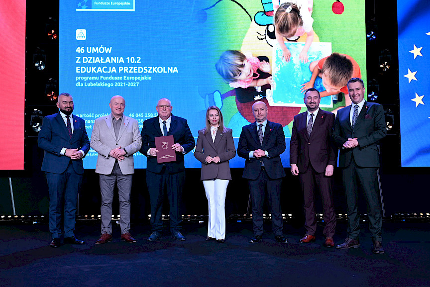 Zarząd Województwa Lubelskiego pozuje do zdjęcia z beneficjentem projektu. Mężczyzna trzyma teczkę w umową.