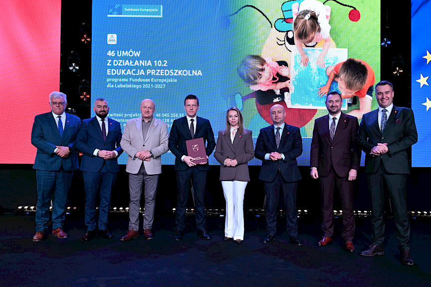 Zarząd Województwa Lubelskiego pozuje do zdjęcia z beneficjentem projektu. Mężczyzna trzyma teczkę w umową.