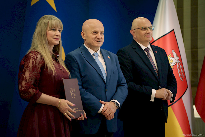 Marszałek Jarosław Stawiarski pozuje do zdjęć z Dyrektorem Wojewódzkiego Urzędu Pracy w Lublinie Piotrem Pitucha oraz Beneficjentką projektu trzymającą teczkę z umową.