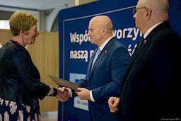 Marszałka Województwa Lubelskiego Jarosława Stawiarskiego podaje rękę w ramach gratulacji beneficjentce projektu. Obok niego stoi Dyrektor Wojewódzkiego Urzędu Pracy w Lublinie Piotr Pitucha.