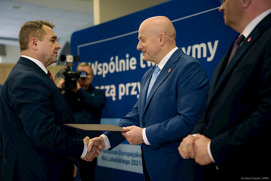 Marszałka Województwa Lubelskiego Jarosława Stawiarskiego podaje rękę w ramach gratulacji beneficjentowi projektu. Obok niego stoi Dyrektor Wojewódzkiego Urzędu Pracy w Lublinie Piotr Pitucha.
