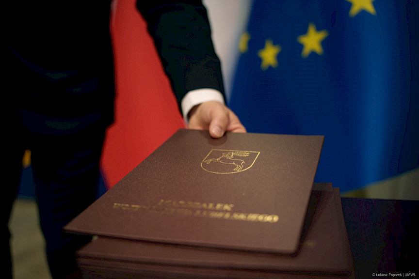 Ujęcie stosu bordowych teczek ze znakiem województwa lubelskiego koziołkiem oraz napisem złotymi literami Marszałek Województwa Lubelskiego.