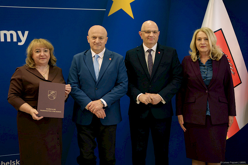 Marszałek Jarosław Stawiarski pozuje do zdjęć z Dyrektorem Wojewódzkiego Urzędu Pracy w Lublinie Piotrem Pitucha oraz Beneficjentką projektu trzymającą teczkę z umową.