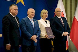 Marszałek Jarosław Stawiarski pozuje do zdjęć z Dyrektorem Wojewódzkiego Urzędu Pracy w Lublinie Piotrem Pitucha oraz Beneficjentką projektu trzymającą teczkę z umową.