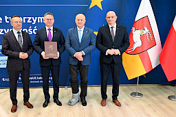 Marszałek Jarosław Stawiarski pozuje do zdjęć z Dyrektorem Wojewódzkiego Urzędu Pracy w Lublinie Piotrem Pitucha oraz Beneficjentem projektu trzymającym teczkę z umową.