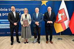 Marszałek Jarosław Stawiarski pozuje do zdjęć z Dyrektorem Wojewódzkiego Urzędu Pracy w Lublinie Piotrem Pitucha oraz Beneficjentką projektu trzymającą teczkę z umową. Obok kobiety stoi mężczyzna.