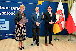 Marszałek Województwa Lubelskiego Jarosław Stawiarski pozuje do zdjęć z Beneficjentką projektu trzymającą teczkę z umową. Obok nich stoi Dyrektor Wojewódzkiego Urzędu Pracy Tomasz Pitucha.